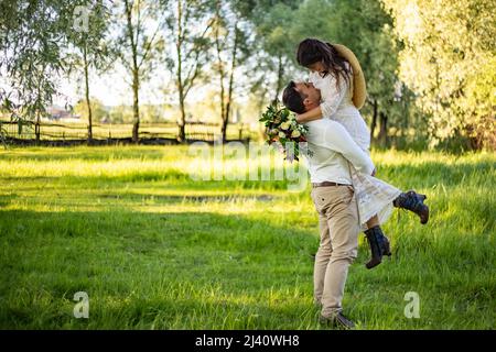 Elégante mariée heureuse, tenue de marié prise dans les mains et danse. Le marié se lève et fait tourner la mariée. Les jeunes mariés s'embrassent. Sur le fond de la nature dans la co Banque D'Images