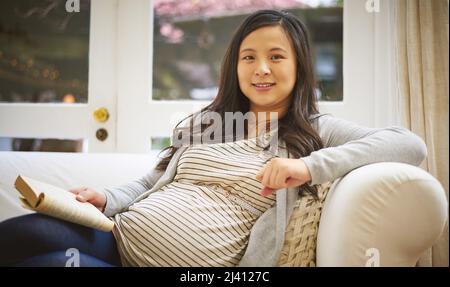 Ce livre est un must-read pour toute maman attendue. Portrait d'une femme enceinte lisant un livre à la maison. Banque D'Images