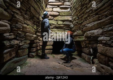 Un mâle et une femelle touristes regardent vers un puits de lumière à l'intérieur du Quoyness Néolithique Chambered Cairn sur Sanday, Orkney. Banque D'Images