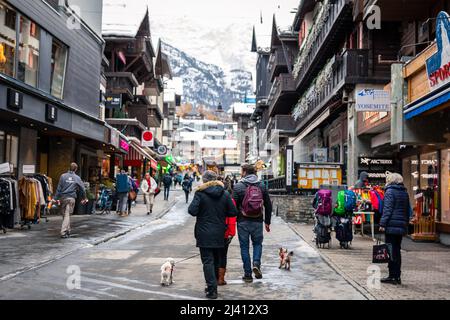 Zermatt, Suisse - 11 novembre 2019: Touristes marchant avec des chiens dans la rue à l'intérieur de la vieille ville entourée d'anciens bâtiments de magasin, restaurant, h Banque D'Images