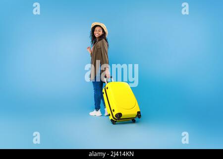 Portrait complet de la bonne femme noir marchant avec une valise sur fond bleu de studio, espace de copie Banque D'Images
