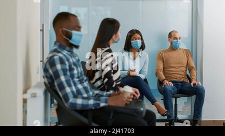 Groupe multiethnique de candidats recevant des documents d'emploi, se préparant à commencer une entrevue d'emploi avec le service des RH. Les gens qui attendent dans le hall d'entrée pour assister à une réunion pendant une pandémie. Banque D'Images