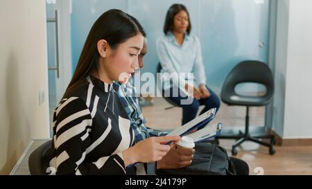 Le candidat lit les renseignements sur la sélection sur papier et attend dans le hall, se prépare à l'entrevue d'emploi avec le recruteur des RH. Femme avec une opportunité de carrière regardant CV CV CV, emploi. Banque D'Images