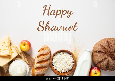 Carte de vœux Happy Shavuot. Flat Lay produits laitiers, bouteille de lait, blé, pain, pommes sur fond blanc. Banque D'Images