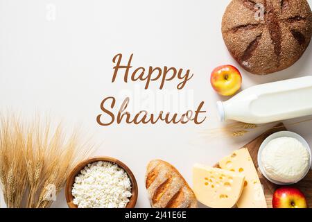 Carte de vœux Happy Shavuot, bannière, affiche. Arrière-plan de vacances juives. Produits laitiers, bouteille de lait, fromage cottage, pain, fromage, pommes, blé o Banque D'Images