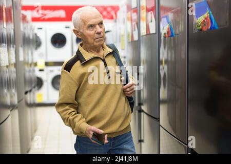 homme âgé à la recherche d'un réfrigérateur au comptoir dans la salle d'exposition du service d'hypermarché des appareils électriques Banque D'Images