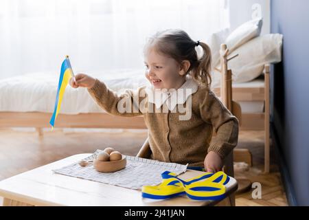 bonne fille portant un drapeau ukrainien près du ruban bleu et jaune et des jouets en bois sur le bureau Banque D'Images