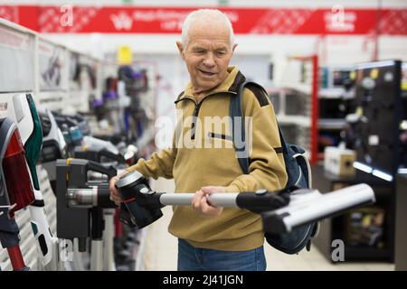 Un homme âgé qui choisit un aspirateur vertical dans la salle d'exposition du magasin d'appareils électriques Banque D'Images