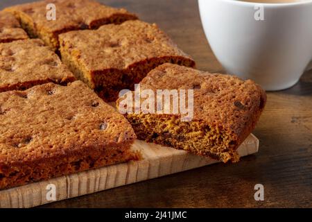 Barres de dessert Blondie Brownie aux pépites de chocolat, un gros plan sur un fond de bois rustique foncé avec une tasse de thé Banque D'Images