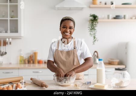 Joyeux jeune femme africaine américaine chef blogueur en tablier faisant de la pâte à tarte Banque D'Images