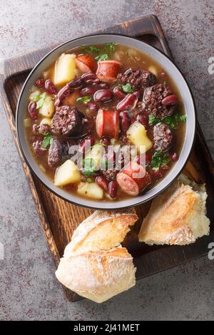 La recette traditionnelle de Sopa da Pedra combine des haricots rouges, des pommes de terre, de la viande séchée et des saucisses dans l'assiette sur la table. Vue verticale du dessus avant Banque D'Images