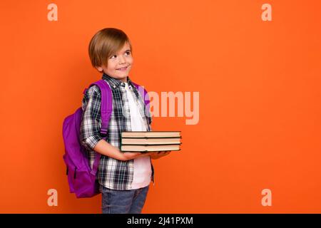 Profil côté photo de jeune garçon curieux penser intelligent look vide tenir l'encyclopédie livre isolée sur fond de couleur orange Banque D'Images