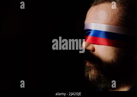 Homme avec le drapeau russe aveuglement sur fond noir, la propagande russe fermé les yeux des gens concept. Banque D'Images