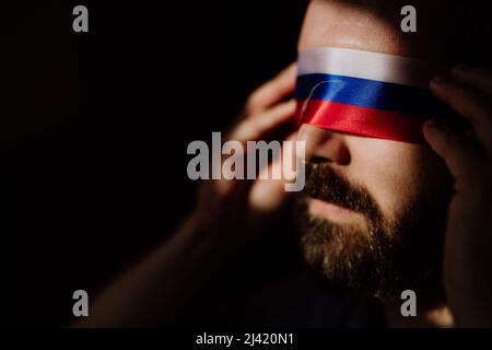 Homme avec le drapeau russe aveuglement sur fond noir, la propagande russe fermé les yeux des gens concept. Banque D'Images