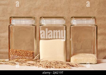 Riz, sarrasin, semoule, grains dans les pots en verre transparent sur la table de cuisine. Modèle de fond de cuisine et de nourriture rurale Banque D'Images