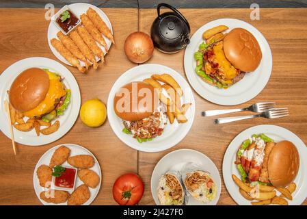 Plats de restauration rapide avec divers hamburgers, frites maison, queues de crevettes tempura, croquettes maison avec sauce tomate, ailes de poulet, burrito avec ri Banque D'Images