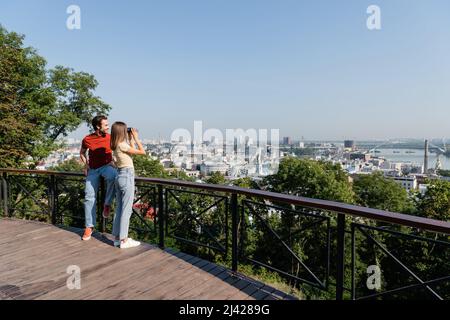 Femme regardant à travers des jumelles près d'un petit ami souriant sur le point de vue de la ville Banque D'Images