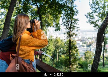 Vue latérale de la jeune femme avec sac à dos regardant à travers des jumelles près de l'extérieur de petit ami Banque D'Images