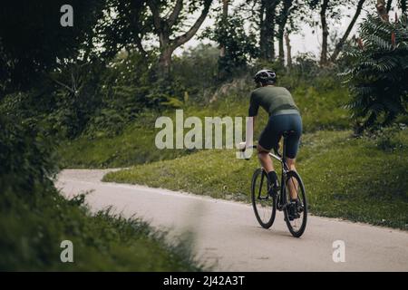 Jeune homme sportif portant un casque de protection à vélo noir au parc vert de la ville. Homme actif appréciant son passe-temps préféré sur l'air frais. Concept de santé l Banque D'Images