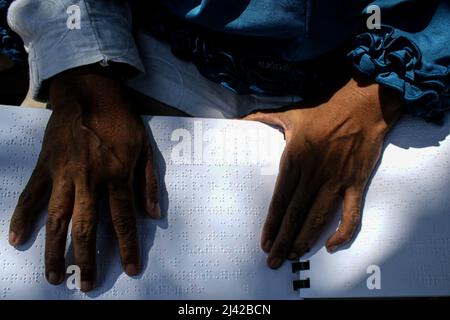 Surabaya, Indonésie. 11th avril 2022. Une femme malvoyante lit Quran écrit en braille à un arrêt de bus avant de participer à une visite en bus du Ramadan pendant le mois Saint du Ramadan à Surabaya, Java-est, Indonésie, le 11 avril 2022. La lecture de Coran écrit en braille dans les transports publics fait partie d'une campagne visant à appeler à un accès amical pour les personnes handicapées. Credit: Kurniawan/Xinhua/Alay Live News Banque D'Images