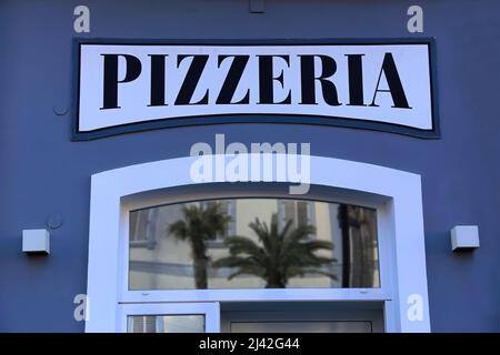 Panneau du restaurant pizza au-dessus de la porte d'entrée, face à une façade bleue Banque D'Images