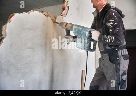 Gros plan d'un instrument à main puissant spécial avec mécanisme à percussion pour le forage et la découpe des murs. Homme tenant le marteau et démontant la paroi interne dans la pièce. Banque D'Images