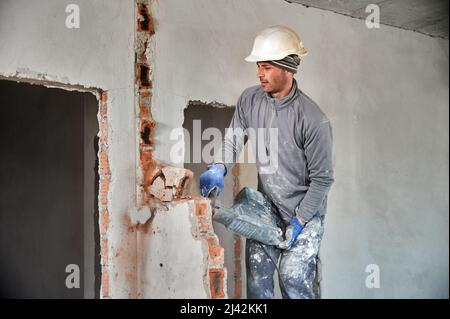 Travailleur dans un casque de protection avec perforateur achèvement de la déconstruction du reste du mur de briques à l'intérieur de la pièce. Le constructeur fait des travaux de réparation sur le démontage des murs et des cloisons. Banque D'Images