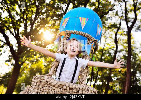 garçon aux cheveux bouclés dans un panier de ballon bleu sourit et regarde dans la distance avec le fond de verdure et le soleil. Banque D'Images