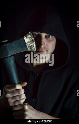 Portrait d'un jeune homme à capuchon avec des yeux bleus qui avec une hache dans sa main a un regard inquiétant Banque D'Images