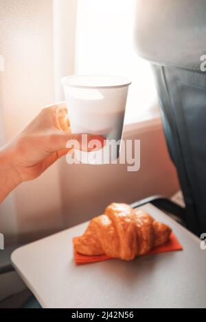 Une jeune fille mange un croissant et boit du café assis près de la fenêtre sur un avion et vole en vacances Banque D'Images