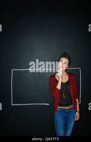 Les meilleures idées sont créées en dehors de la boîte. Photo studio d'une jeune femme réfléchie posant avec une craie d'illustration d'une boîte contre une obscurité Banque D'Images