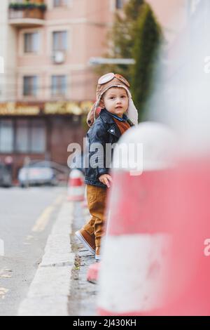 Un garçon élégant de 3 ans dans une veste en cuir et un pantalon marron marche dans la rue. Enfant moderne. Mode pour enfants. Enfant heureux Banque D'Images