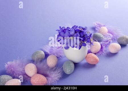 Concept joyeuses Pâques. Oeufs de Pâques avec fleurs d'hepatica et plumes sur fond violet. Banque D'Images
