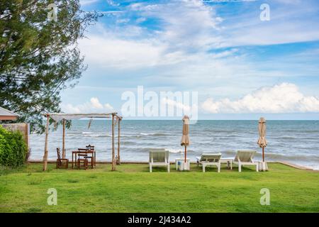Chaise longue en bois avec parasol fermé et belvédère sur pelouse verte dans la mer tropicale et ciel bleu en été Banque D'Images