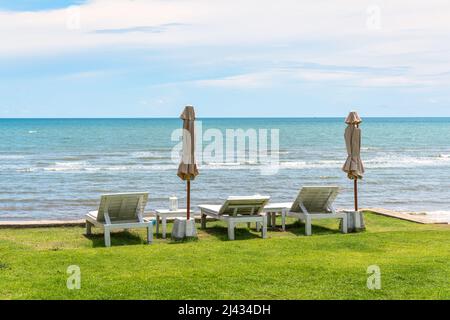 Chaise longue en bois avec parasol fermé et belvédère sur pelouse verte dans la mer tropicale et ciel bleu en été Banque D'Images
