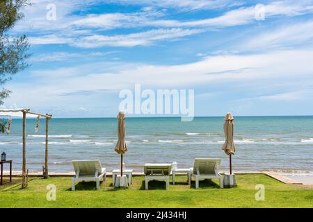 Chaise longue en bois avec parasol fermé et belvédère sur pelouse verte dans la mer tropicale et ciel bleu en été Banque D'Images