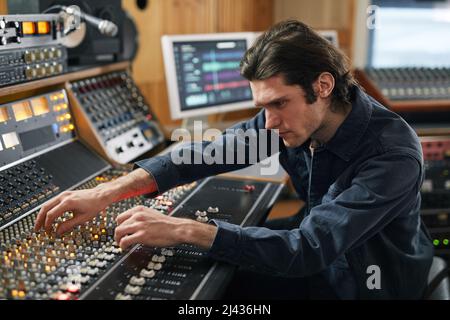 Vue latérale du producteur de musique à l'aide d'une station de travail audio numérique dans un studio d'enregistrement professionnel Banque D'Images