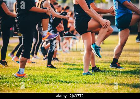 Groupe courant chaud, jambes sur la belle herbe verte dans la lumière chaude. Entraînement en équipe, étirement et exercice de base Banque D'Images