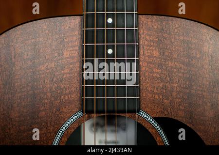 Un gros plan de la partie supérieure d'une guitare acoustique montrant le tableau de bord, les frets, les marqueurs de position, les cordes, la rosette, pickguard et trou sonore. Banque D'Images