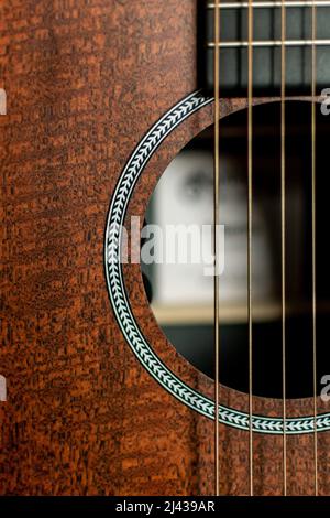Un gros plan rogné du corps d'une guitare acoustique en bois avec les cordes en acier et le trou sonore visible Banque D'Images