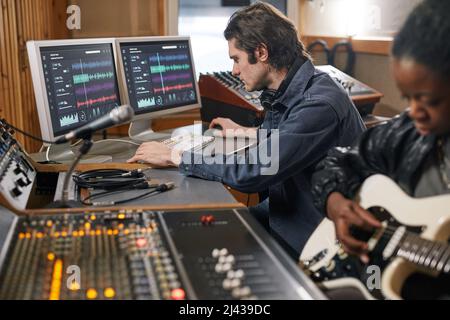 Vue latérale chez un musicien masculin sur une station de travail audio dans un studio d'enregistrement professionnel, espace de copie Banque D'Images
