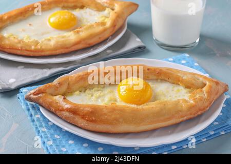 Khachapuri à Adjarian, tartes ouvertes avec du fromage suluguni et du jaune d'œuf sous forme de bateau sur des assiettes sur fond bleu, cuisine traditionnelle géorgienne Banque D'Images