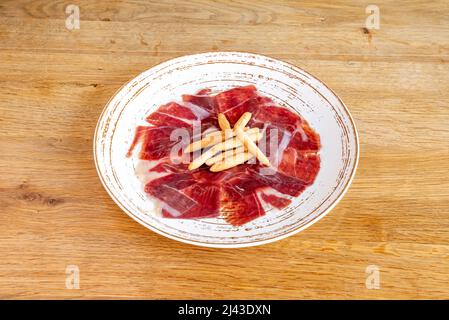 Tapas au jambon nourri à l'Acorn avec croûtons sur une assiette blanche sur une table en bois Banque D'Images