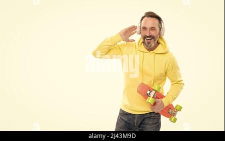 joyeux homme mature skateboarder écouter de la musique porter des écouteurs tenir penny skateboard, dans la rue. Banque D'Images
