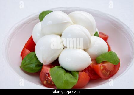 Cuisine italienne, savoureuse salade de caprese avec tomates cerises rouges, fromage mozzarella blanc et feuilles de basilic vert Banque D'Images