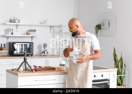 Beau homme fouetter l'œuf en albumine avec le mélangeur tout en suivant la vidéo de cuisine tutoriel dans la cuisine Banque D'Images