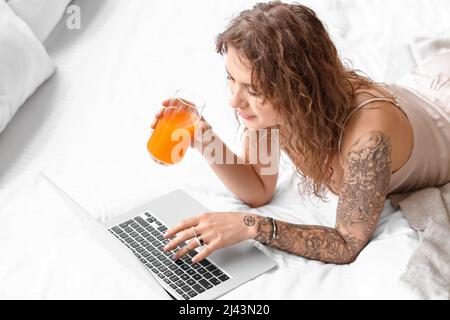 Belle femme tatouée avec un ordinateur portable buvant du jus dans la chambre Banque D'Images