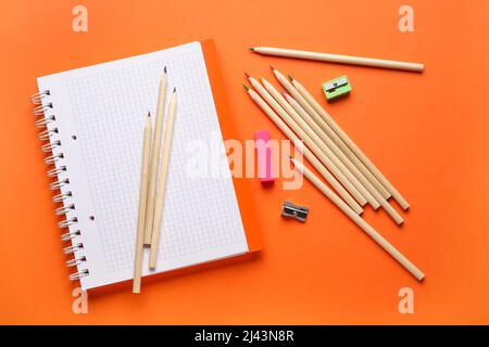 Crayons colorés, carnet vierge et taille-crayons sur fond orange Banque D'Images