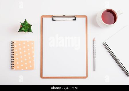 Bureau blanc avec presse-papiers, tasse de thé, crayon, carnet et plante succulente. Flat lay, vue de dessus, maquette. Banque D'Images