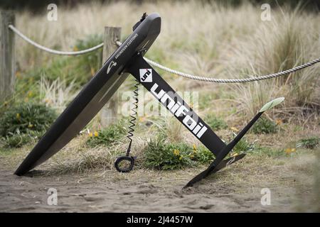 Une planche de surf hydrofoil en fibre de carbone avec hydrofoil en fibre de carbone et laisse se trouve sur le sable à Piha Beach, Auckland, Nouvelle-Zélande. Banque D'Images